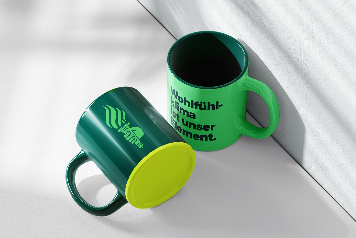 Zwei Vestair-Tassen in Dunkelgrün - auf einer ist das Icon einer Hand, die eine Fackel hält, auf der anderen ein Claim
